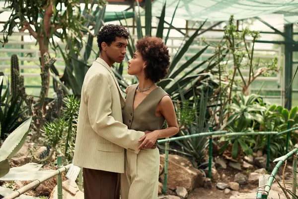 Um casal abraça ternamente entre plantas diversas em um belo cenário de estufa. — Fotografia de Stock