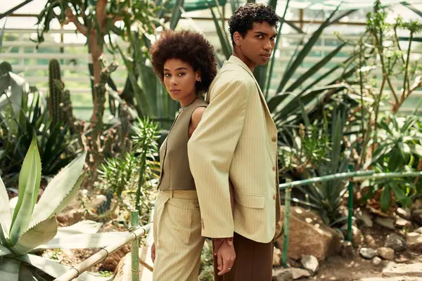 A young couple stands back to back in a lush, vibrant greenhouse. — Stock Photo