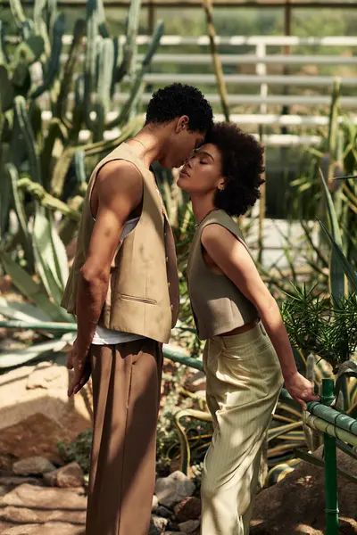 Abraçando em uma estufa iluminada pelo sol, um jovem casal expressa seu amor em meio a plantas vibrantes. — Fotografia de Stock