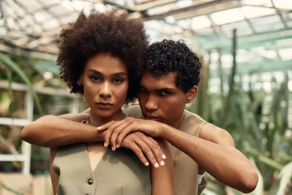 Loving couple shares an intimate moment amidst lush plants in a serene greenhouse atmosphere. — Stock Photo