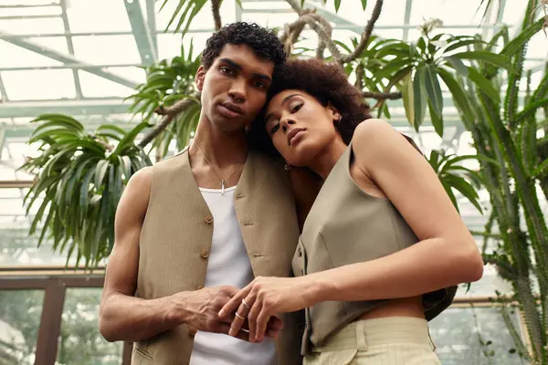 Deux jeunes individus s'embrassent chaleureusement au milieu de plantes vibrantes et de verdure sereine dans une serre. — Photo de stock