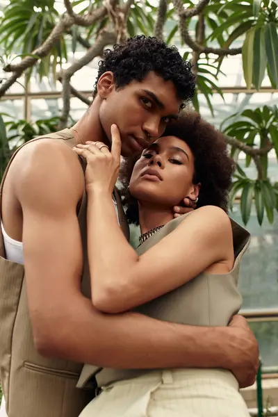 Una pareja amorosa está cerca en un invernadero lleno de plantas vibrantes, sonriendo suavemente. - foto de stock