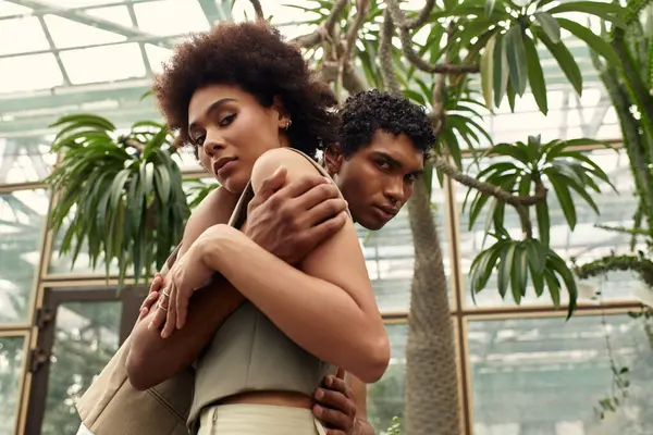 Loving couple shares an intimate moment in a greenhouse filled with thriving plants and foliage. — Stock Photo