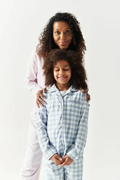 Black mother hugs daughter in matching PJs, grey background. — Stock Photo