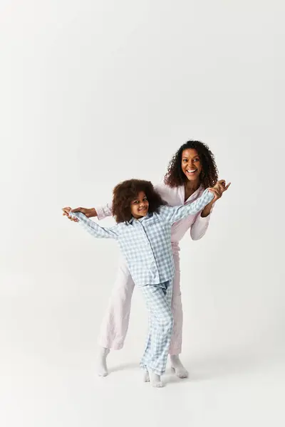 A joyful African American mother and daughter share a playful dance in their pajamas in a studio. — Stock Photo