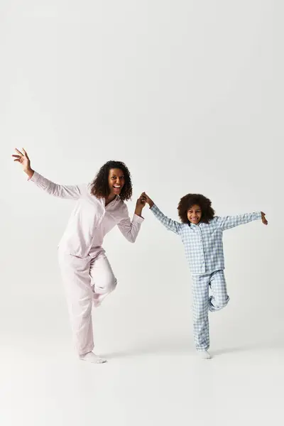 Una madre e una figlia afroamericane ballano gioiosamente indossando pigiami coordinati. — Foto stock