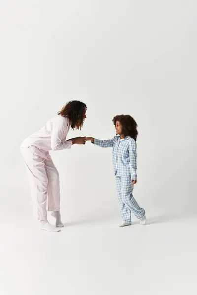 In studio, African American mother and daughter in pyjamas holding hands. — Stock Photo