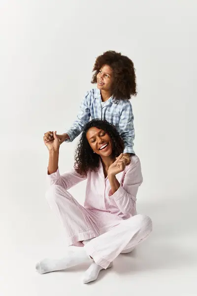 Black mom smiles, while holding hands with her child, both in PJs. — Stock Photo