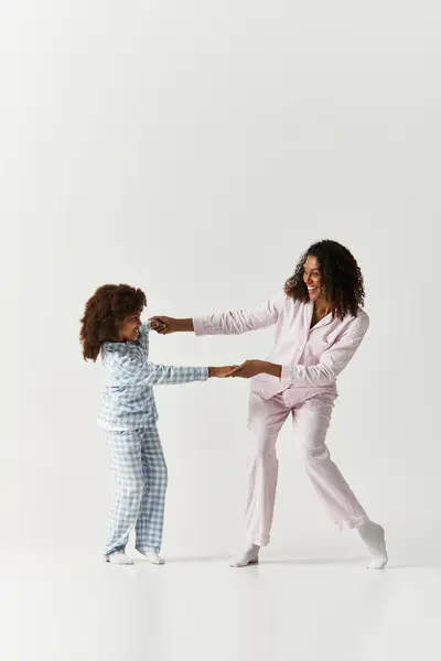 Mãe e filha felizes dançando e de mãos dadas, ambos em PJs correspondentes. — Fotografia de Stock