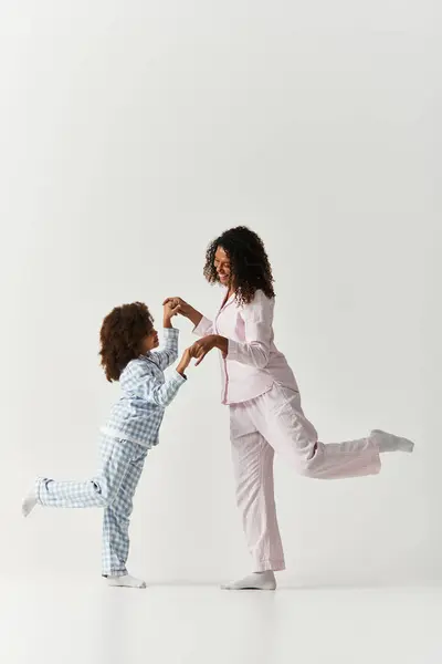Una felice madre e figlia afroamericana condividono un momento, in equilibrio su una gamba in pigiama. — Foto stock
