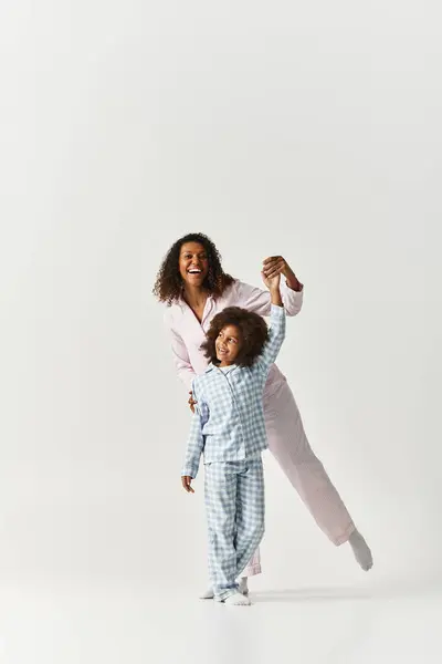 Black mom and cute daughter in PJs dancing on grey background — Stock Photo