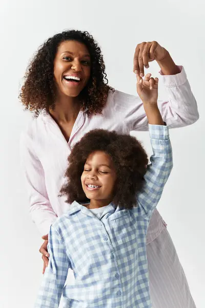 African American mother and daughter wearing pyjamas together, laughing in a grey studio. — Stock Photo