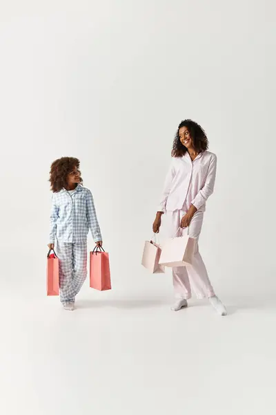 Nero madre e figlia in corrispondenza PJs con shopping bags. — Foto stock