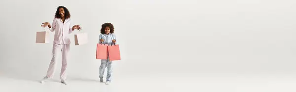 Sorrindo mãe e filha negra em pijama combinando segurar sacos de compras, banner — Fotografia de Stock