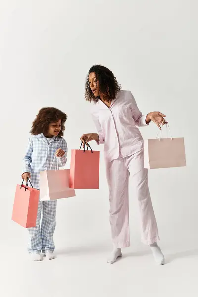Madre e figlia afroamericana in pigiama abbinato, con borse della spesa. — Foto stock