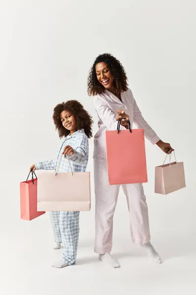 Preto mãe e filha em correspondência PJs, sacos de compras, estúdio. — Fotografia de Stock