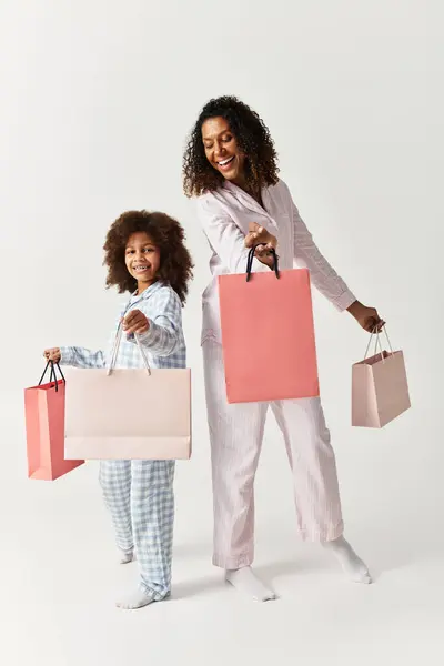 Madre e figlia afroamericana, in pigiama abbinato, posano con borse della spesa in uno studio. — Foto stock
