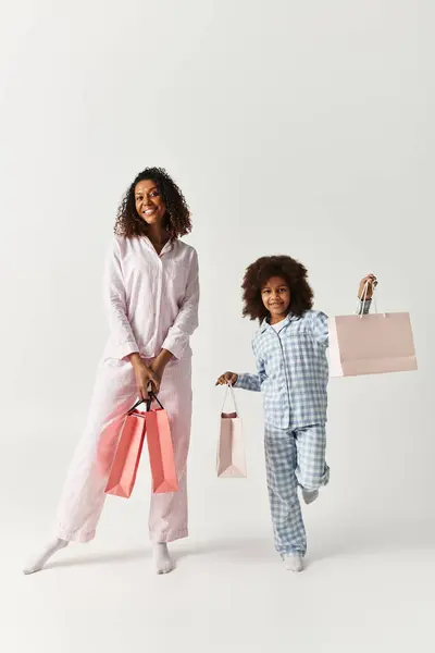 Afroamericano madre e sua figlia in corrispondenza pigiama sono in possesso di shopping bags in un studio. — Foto stock
