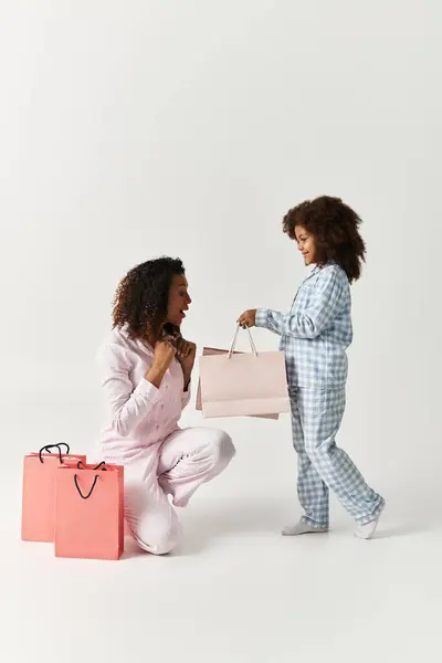 Black mom kneels, surprised by daughters gift bag. — Stock Photo