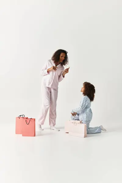 Madre e figlia, entrambe in pigiama abbinato, disimballano allegramente i regali in un ambiente da studio. — Foto stock