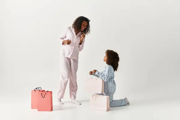 Black mom and daughter in PJs share moment by shopping bags. — Stock Photo