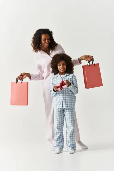 African American mother with daughter in pyjamas shows a gift. Holding shopping bags, family look. — Stock Photo