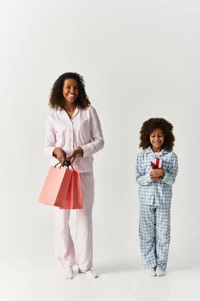 An African American mother holds shopping bags while her daughter clutches a gift in pajamas. — Stock Photo