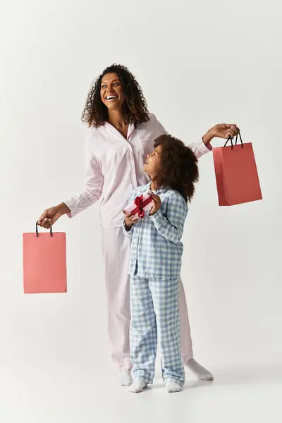 Black mother and daughter in PJs with gifts and shopping bags in studio. — Stock Photo