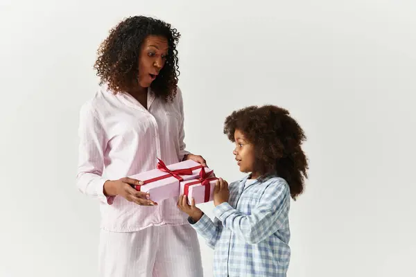 Happy Black daughter gives pink gifts to joyful mom in PJs. — Stock Photo