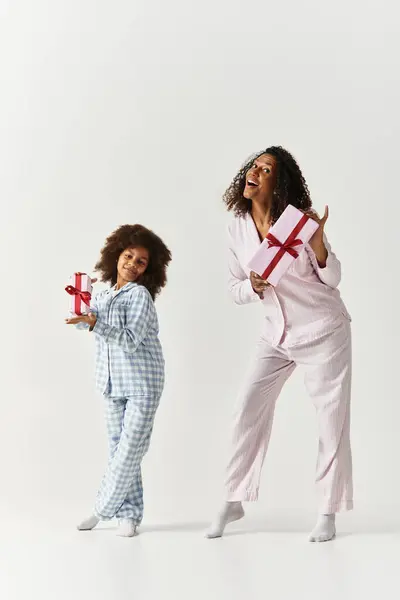 An African American mother and daughter smile while in matching pyjamas and holding gifts. — Stock Photo