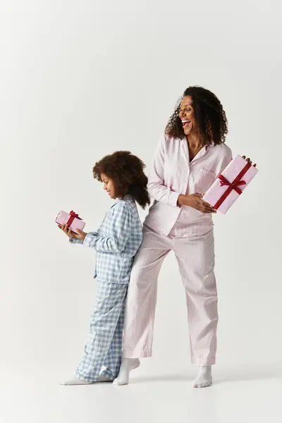 A smiling African American Mother and daughter, dressed in pajamas, show off similar looking gifts. — Stock Photo