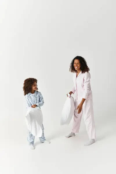 Mother and daughter dressed in pyjamas playfully engage in a pillow fight within the studio. — Stock Photo