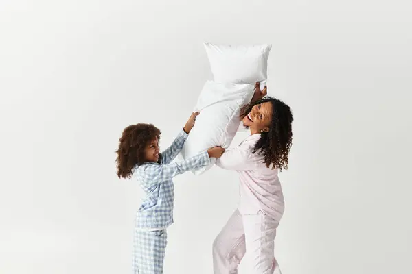 Uma mãe e filha afro-americana riem enquanto brincam brigando com travesseiros. — Fotografia de Stock