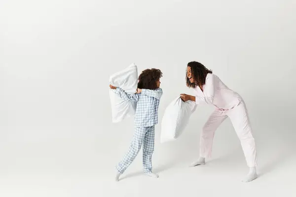 Black mother and daughter pillow fight in matching PJs. — Stock Photo