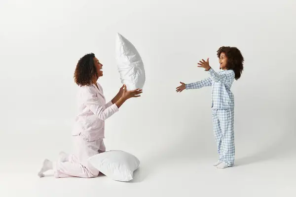 In un ambiente da studio, una madre e una figlia afroamericane giocano con i cuscini. — Foto stock