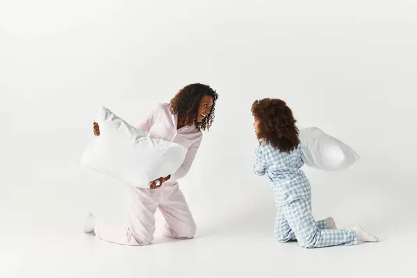 Afro-americano madre e figlia in corrispondenza pigiama giocosamente battaglia fuori con cuscini. — Foto stock