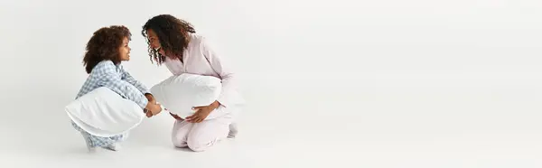 In the studio, a mother and daughter in matching pyjamas are having a playful pillow fight, banner — Stock Photo