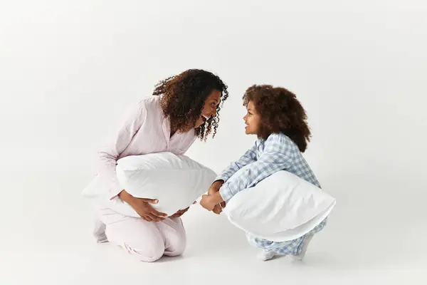 Black mother and daughter holding pillows on grey background. Matching pajamas. — Stock Photo