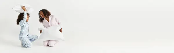 Combinando PJs, mãe e filha travesseiro luta, banner divertido estúdio — Fotografia de Stock