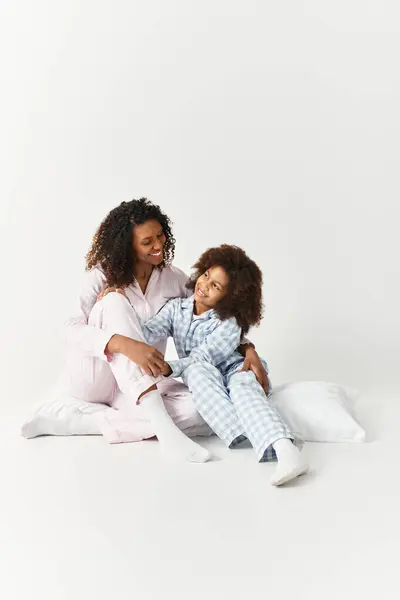 Nero mamma e figlia in pigiama, sorridente e seduta sul pavimento. — Foto stock