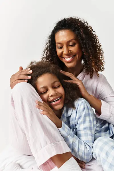 Uma mãe afro-americana segura suavemente a filha. Ambos estão de pijama, sorrindo de alegria. — Fotografia de Stock