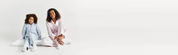 Uma mãe e filha afro-americana vestindo pijama combinando, sentar sorrindo em um estúdio, banner — Fotografia de Stock