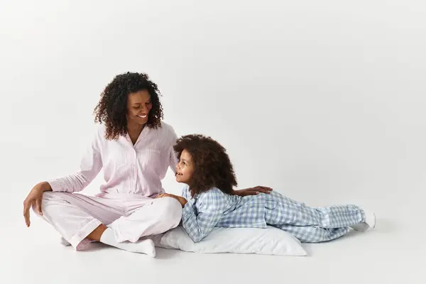 Black mom and daughter in pajamas share loving look. Grey background. — Stock Photo