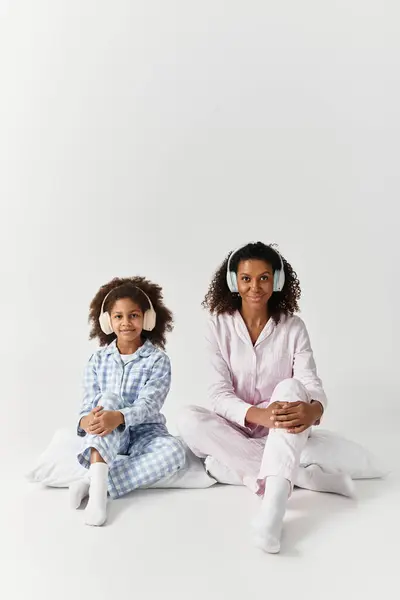 Black mom and daughter in matching PJs listen to music. — Stock Photo
