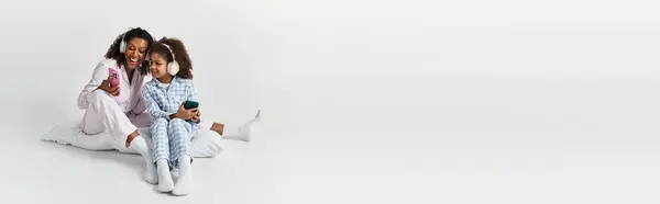 Nero mamma e il suo carino figlia in pigiama guardare telefono in studio banner — Foto stock