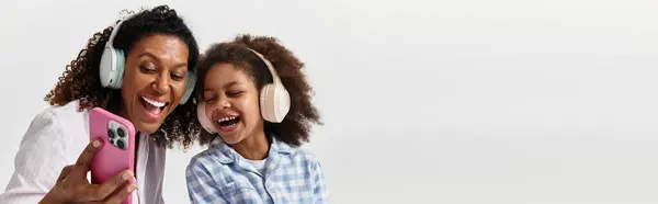 Mother and daughter in matching PJs, laughing and listening to music, banner — Stock Photo