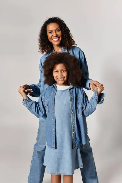An African American mother and her daughter stand side-by-side, smiling in matching denim outfits. — Stock Photo
