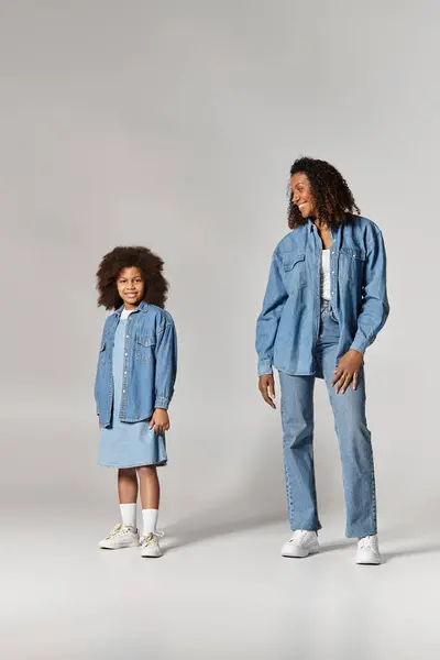 Stylish Black mother and daughter in denim outfits, grey studio. — Stock Photo