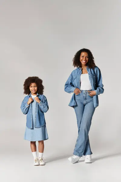 An African American mother and daughter smile in matching denim outfits. — Stock Photo