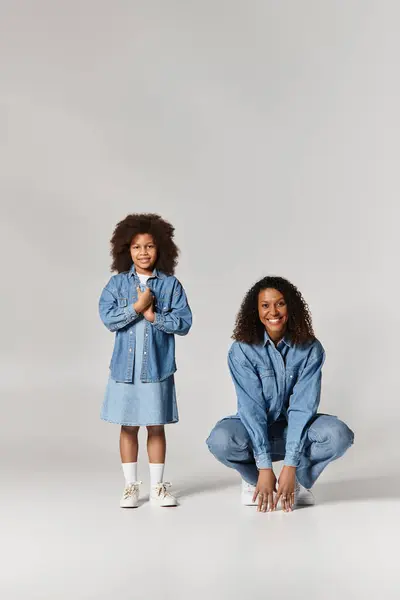 Una madre e una figlia nere posano in abiti di jeans coordinati su uno sfondo grigio. — Foto stock